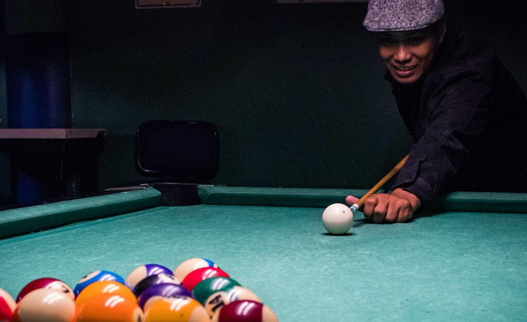 Man with beret smiling while playing billiards